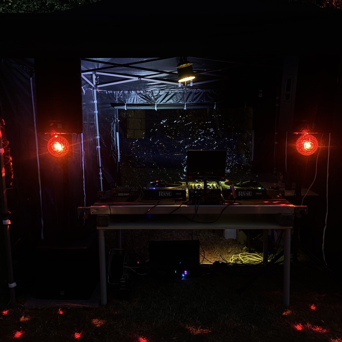 DJ-Pult unter einem Pavillon bei Nacht, flankiert von roten Lampen