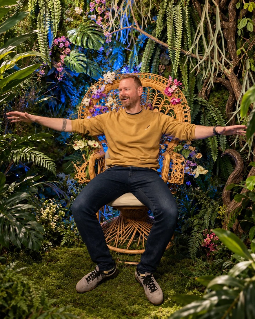 Andreas mit ausgebreiteten Armen in einem Korbstuhl zwischen Pflanzen